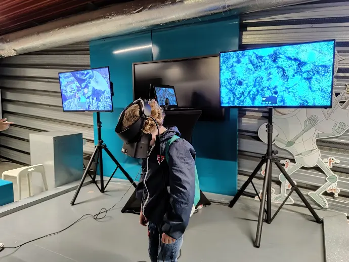 Participant en réalité virtuelle avec manettes et écran de suivi